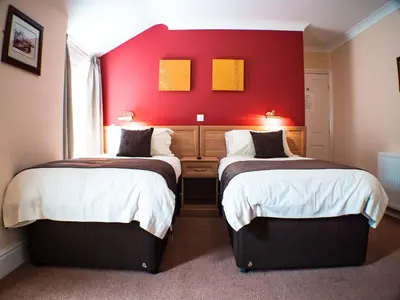 two beds in a room with a red wall at Glen Mona in Douglas