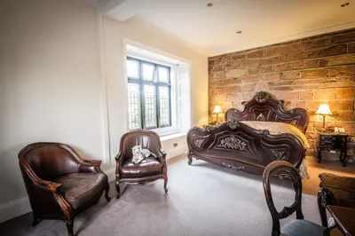 a bedroom with two beds and a chair and a brick wall at Dalston Hall in Carlisle