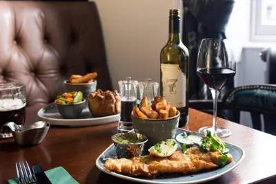a table with a plate of food and a glass of wine at The Ullswater Inn- The Inn Collection Group in Glenridding