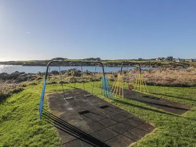 an empty swing set on the grass near the water at The Clamshell in Isle of Whithorn