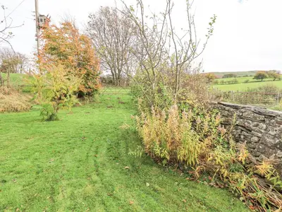 a field with a stone wall and some bushes at The Byre in Cockermouth