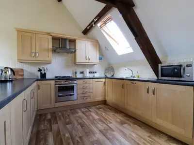 a large kitchen with wooden cabinets and a window at Carpenters Cottage in Cockermouth