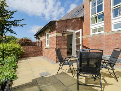 a patio with three chairs in front of a brick house at Carpenters Cottage in Cockermouth