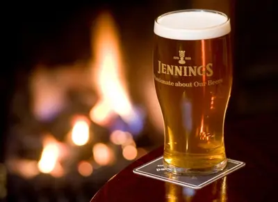 a glass of beer sitting on a table in front of a fire at Lyndhurst in Keswick