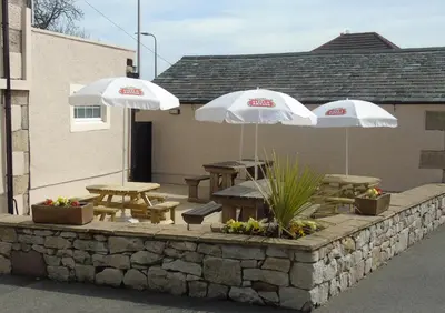 two white umbrellas and picnic tables on a stone wall at The Old Ginn House Inn in Great Clifton