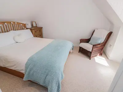 a bedroom with a bed with a blue blanket and a chair at Corrafeckloch Forest Cottages in Bargrennan