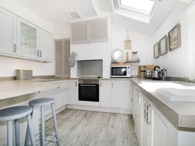 a white kitchen with white cabinets and stools in it at Marsh Villa in Skinburness