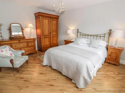 a bedroom with a bed and a chair and a mirror at Bracken Holiday Cottage in Dalbeattie