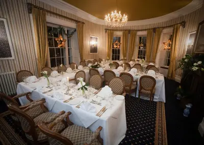 a dining room with white tables and chairs and a chandelier at Overwater Hall in Bassenthwaite