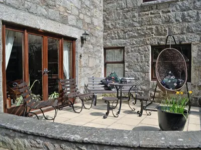 a patio with a table and chairs and a stone building at Anvil in Dalbeattie
