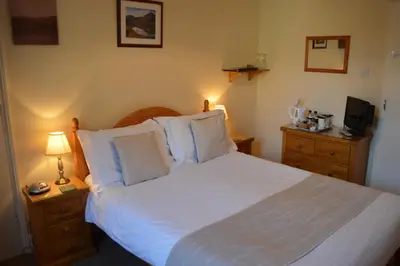 a bedroom with a large bed with white sheets and pillows at Beckside Guest House Keswick in Keswick