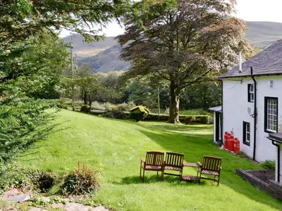 two benches sitting in the grass next to a house at Jose's At The Grange in Mockerkin
