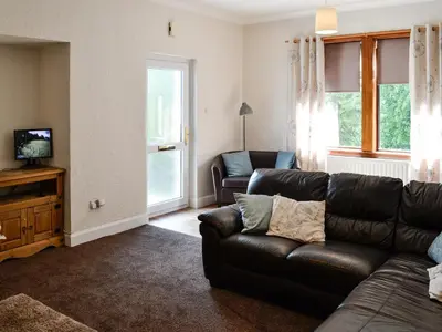 a living room with a leather couch and a television at Brae Cottage in Kelton