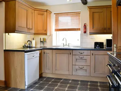 a kitchen with wooden cabinets and a white dishwasher at Farm Cottage in Cleator