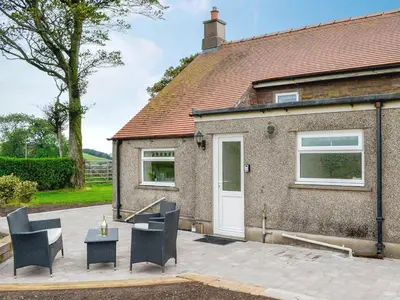 a brick house with chairs and a white door at Rose Cottage in Cleator