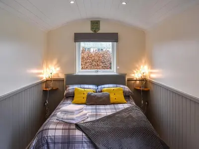 a bedroom with a bed with yellow pillows and a window at Greengill Farm Shepherds Hut- Ukc3632 in Gilcrux