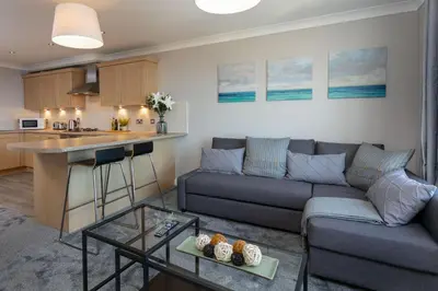 a living room with a couch and a table and a kitchen at Harris Retreat - Donnini Apartments in Ayr