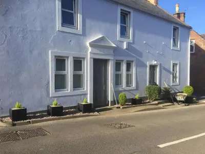 a white house with potted plants in front of it at Vollie House with Hot Tub, Sauna & Log Burner in Penpont