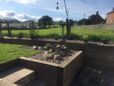 a garden with a retaining wall and a yard at Vollie House with Hot Tub, Sauna & Log Burner in Penpont
