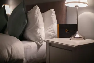 a bed with white pillows and a lamp on a table at Forbes Retreat - Donnini Apartments in Ayr