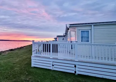 a house with a white fence in front of the water at Ryan Bay Holiday Park in Innermessan