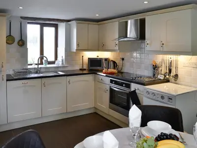 a kitchen with white cabinets and a sink and a table at Swallow Barn in Torpenhow