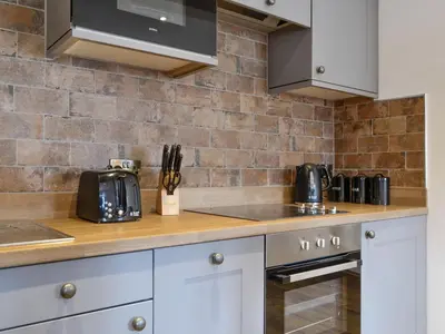 a kitchen with white cabinets and a brick wall at The Byres Tethera in St Bees