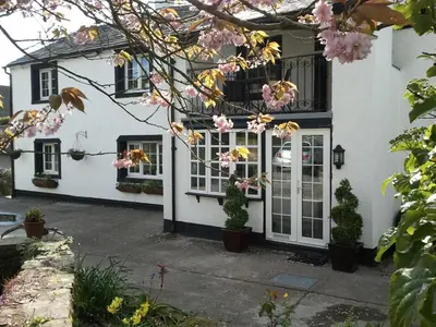 a white house with white doors and pink flowers at Littlebeck Warren in Whitehaven