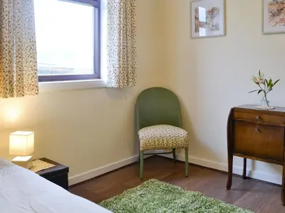 a bedroom with a chair and a dresser and a window at Beuchan Bungalow in Closeburn