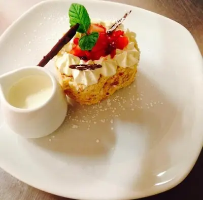 a white plate with a piece of cake with whipped cream at The Fairburn Hotel in Mauchline