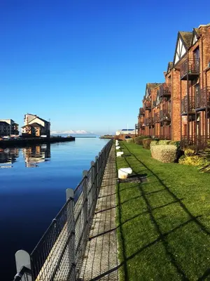 a fence next to a body of water with buildings at The Mariners in Ayr