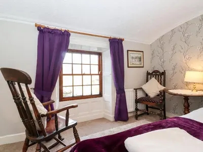 a bedroom with purple curtains and a chair and a window at Castle Lodge in Keswick