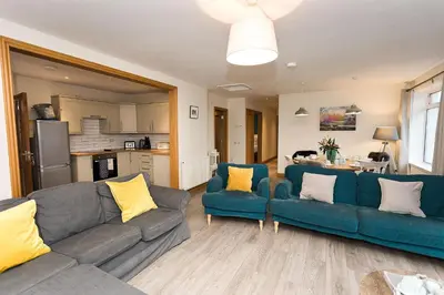 a living room with two blue couches and a kitchen at Fleet View in Gatehouse of Fleet
