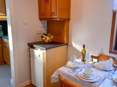 a kitchen with a table with plates and a bottle of wine at Butterhole Cottage in Kelton