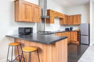 a kitchen with wooden cabinets and a counter with stools at Granary Suite No3 - Donnini Apartments in Ayr