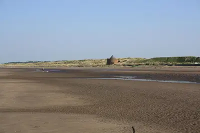 a beach with a person walking on the sand at Fairways Cottages in Prestwick