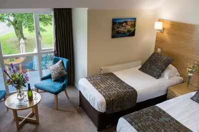 a hotel room with two beds and a chair at Glaramara Hotel in Borrowdale Valley