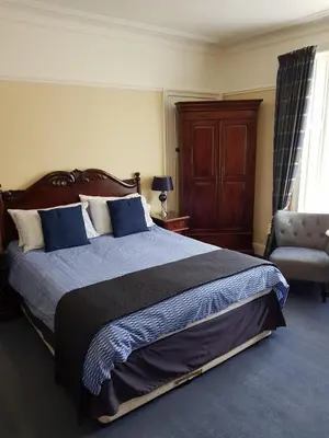 a bedroom with a large bed and a chair at Hamilton House in Dumfries