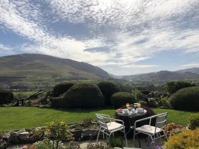 a table and chairs on a lawn with mountains in the background at The Bungalows Guesthouse in Threlkeld