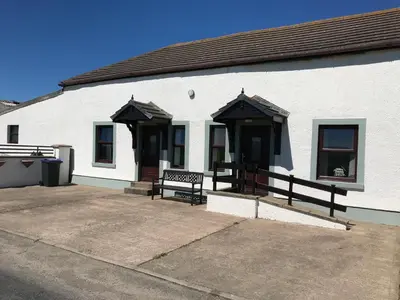 a white building with two benches in front of it at Sea view cottage in Allonby