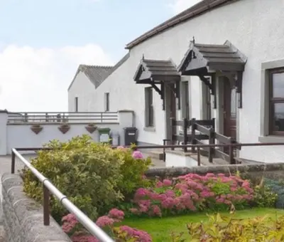 a white building with pink flowers in front of it at Sea view cottage in Allonby