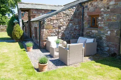 a patio with wicker chairs in front of a stone building at The Nook Cottage in Carlisle