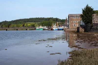 a river with a bridge and boats in the water at The Kirkcudbright Bay Hotel in Kirkcudbright