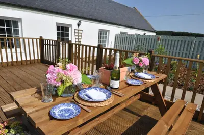 a wooden table with plates and flowers on a deck at No 1 Ramageton at Carnell Estates in Hurlford