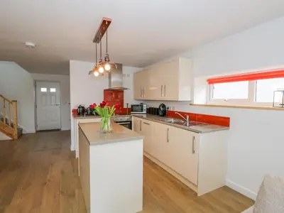 a kitchen with white cabinets and a vase of flowers on a counter at Coney Garth Cottage in Beckermet