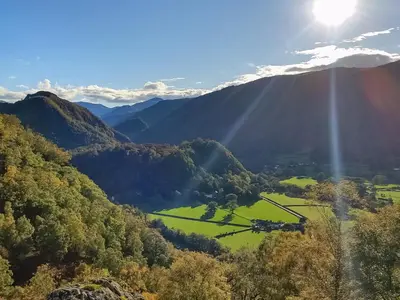 a view of a valley in the mountains with the sun shining at Field House Lodge in Borrowdale Valley