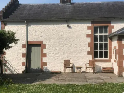 a white brick house with two chairs and a table at The Annex, countryside escape in Dumfries