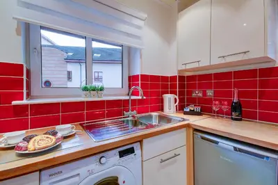 a red tiled kitchen with a sink and a dishwasher at No 7 Ayr Beach - Coorie Doon in Ayr