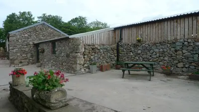 a stone building with a bench and a stone wall at Row Farm Cottage in Millom