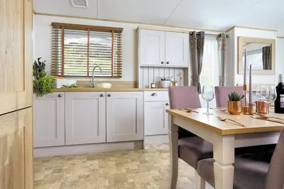 a kitchen with white cabinets and a wooden table at Platinum Holiday Caravan in Bothel